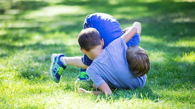 Two young boys wrestling in grass